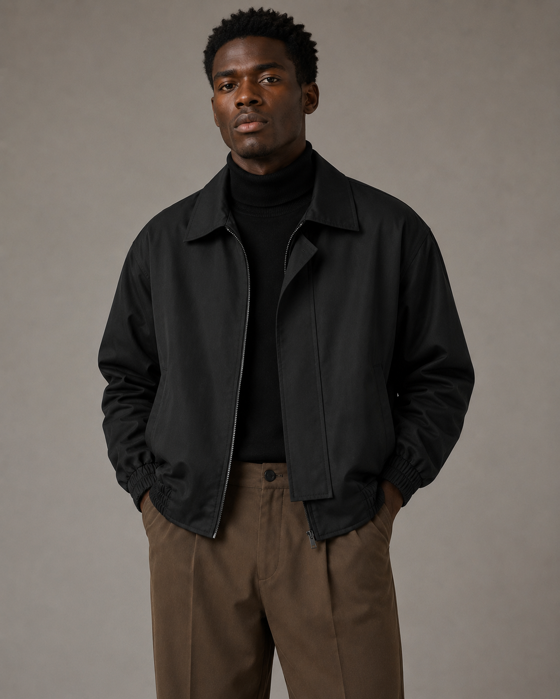Black male model wearing a black lapel zip jacket with dark brown trousers in a professional studio