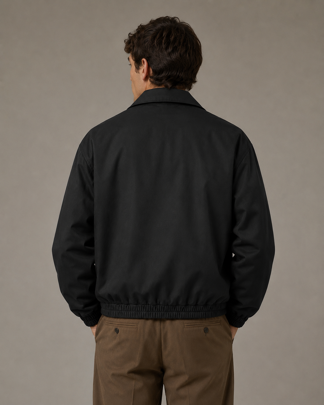 Male model wearing a black lapel zip jacket with dark brown trousers, back view in a professional studio