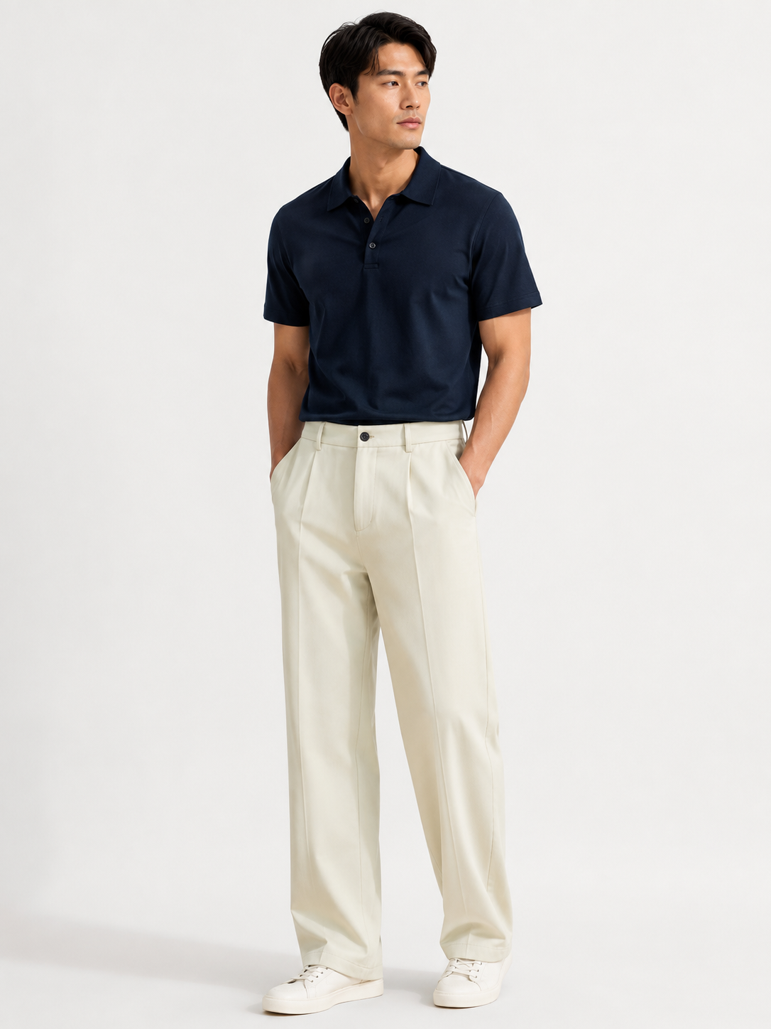 Male model wearing apricot straight-leg loose casual pants with a dark navy polo on a white studio background