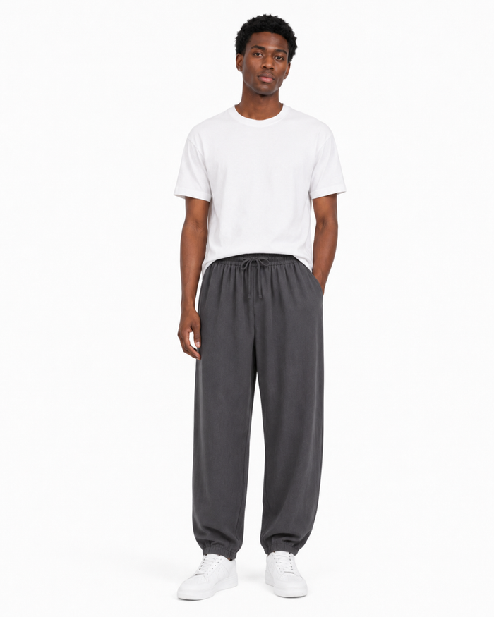 Dark gray relaxed tapered drawstring pants worn by a Black male model on white background